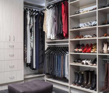 Walk-in closet with clothes hanging and shoe shelves and an ottoman