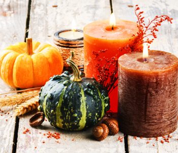 Close up of pumpkins and candles on a white, hardwood floor.