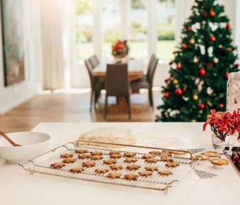 A close up of a kitchen counter with a tray of baked cookies with a Christmas tree in the background.